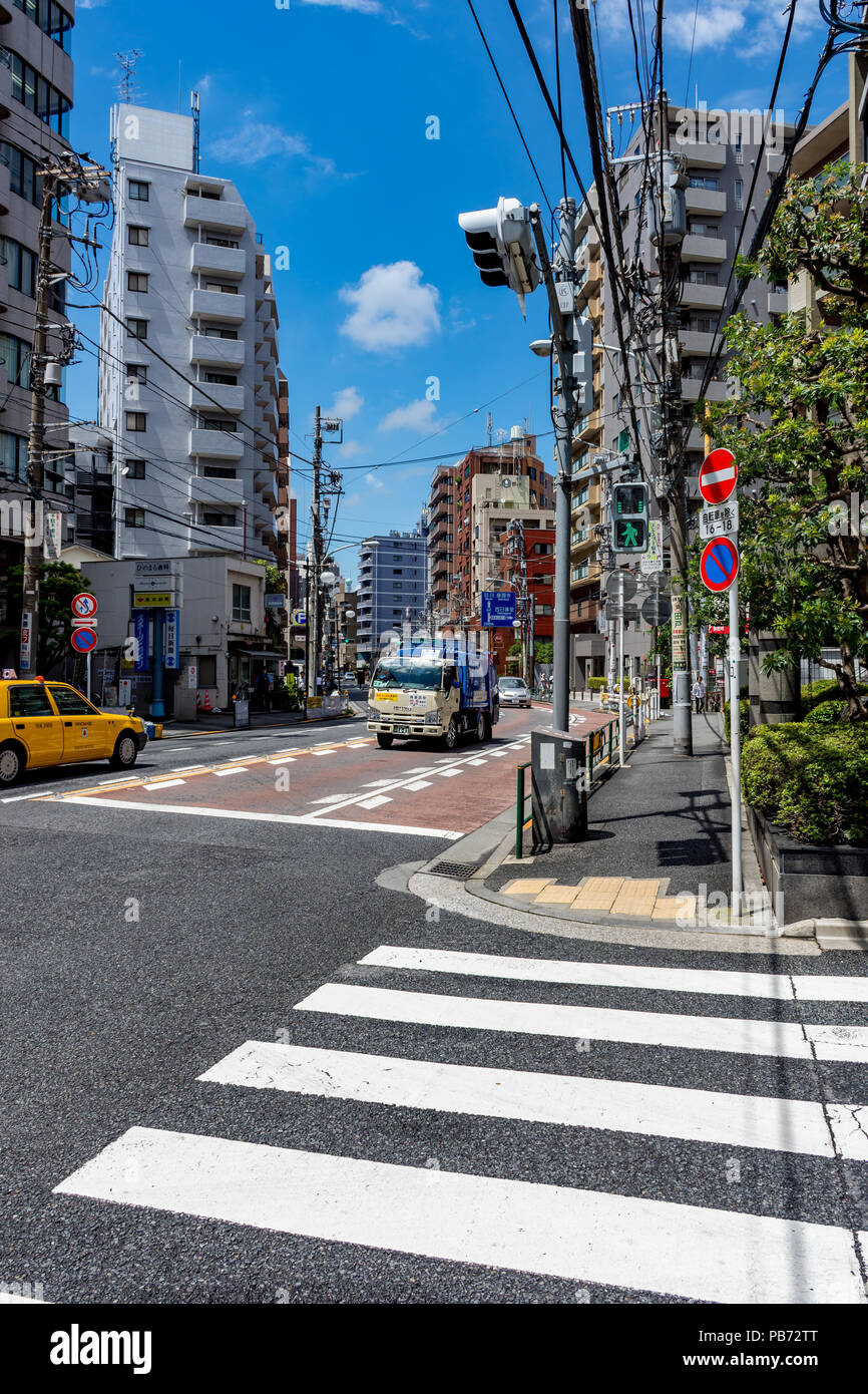 Pedestrian (zebra) crossing on street corner in Tokyo, Japan with yellow taxi, green man sign and blue skies Stock Photo