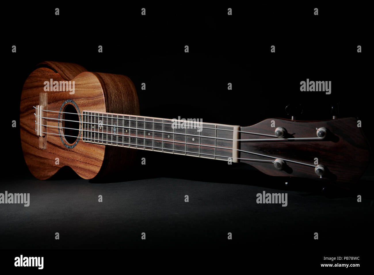 Traditional koa wood ukulele. Hawaiian uke musical instrument. Full body and neck against black background with copy space. Stock Photo