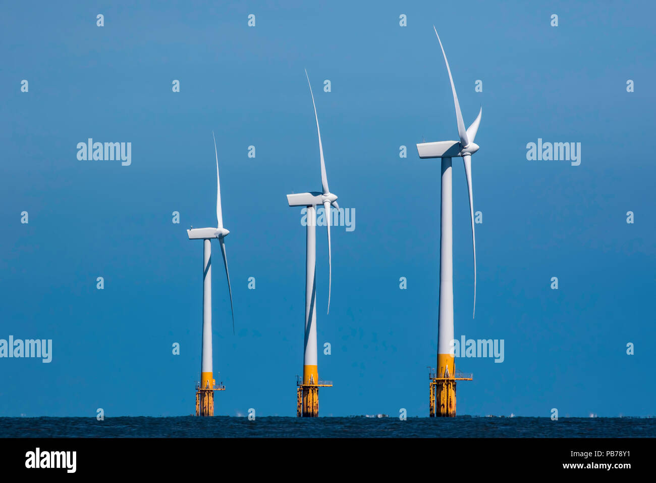 The rise of environmentally-friendly wind power.  Offshore clean energy wind farm. Three synchronised wind power turbines in profile ascending height. Stock Photo