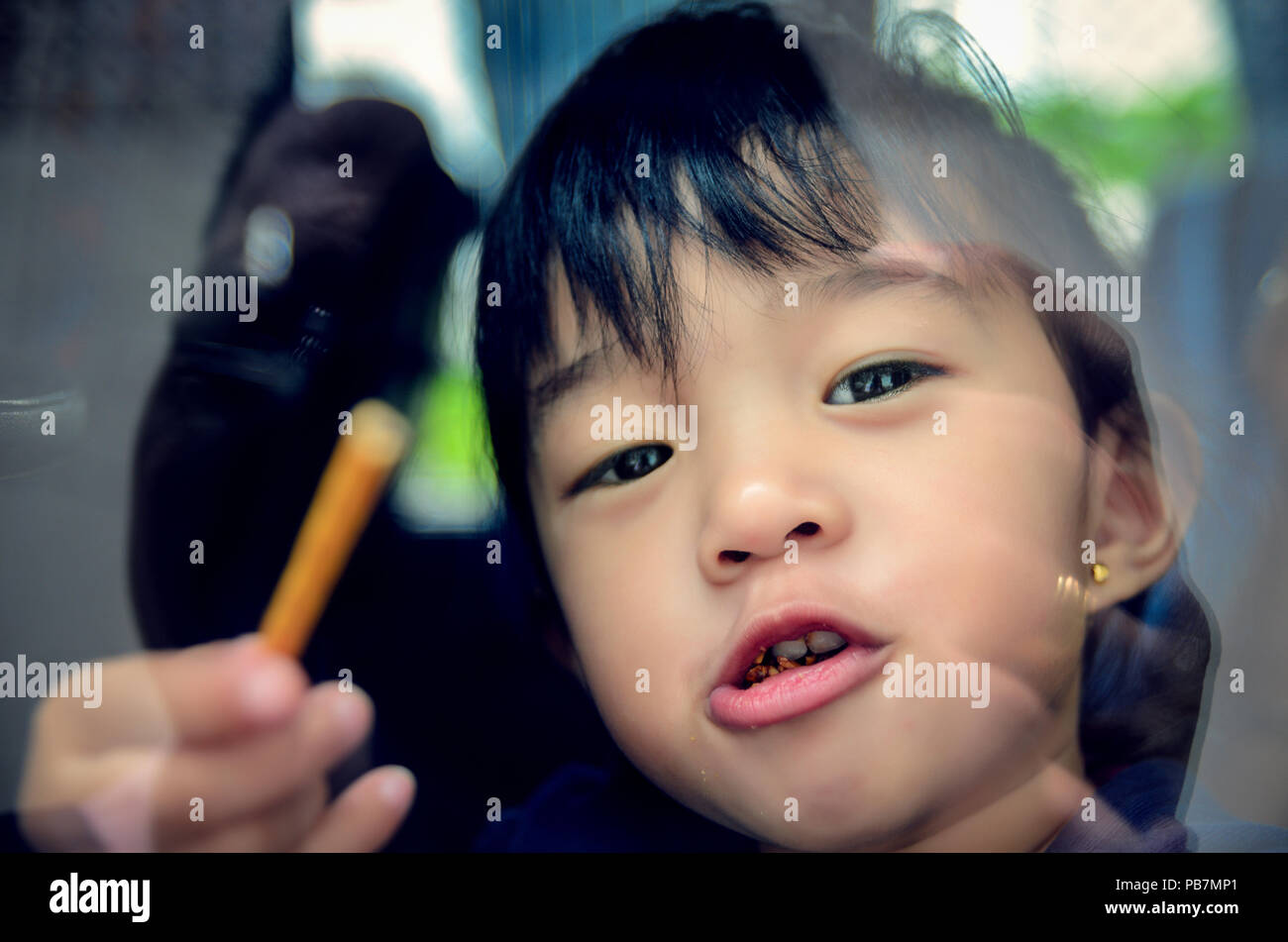 Girl behind the glass window looking outside eating some snacks Stock Photo