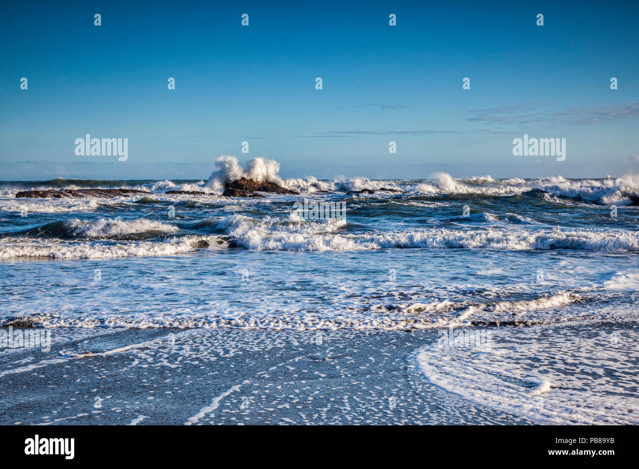 Waves rushing at the shore and splashing over rocks just before high tide. Stock Photo
