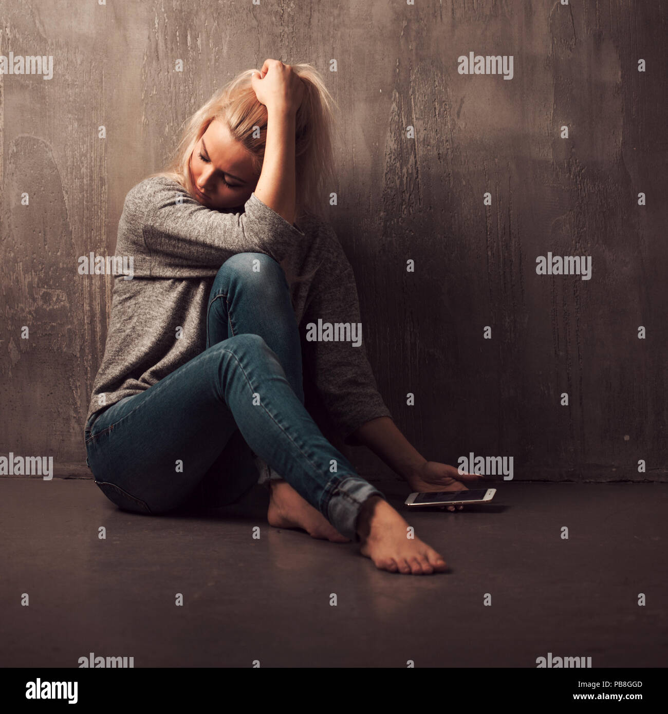 Helpline, psychological assistance. Suffering young woman sitting in a corner with a phone in her hand. mental health, grey background Stock Photo