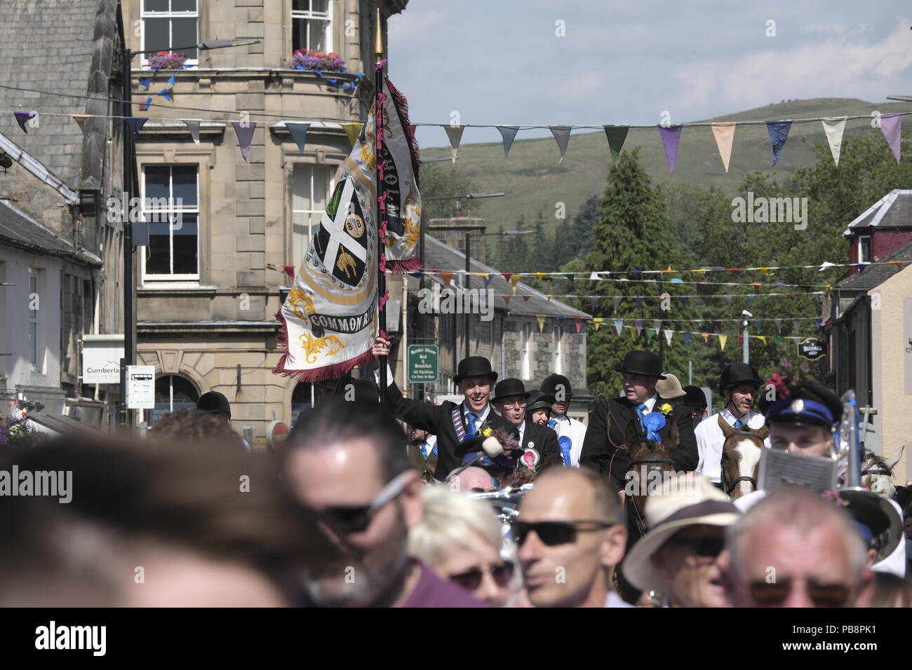 Langholm, Scotland, UK. 27th July, 2018.    Langholm Common Riding - 'Langholm's Great Day' Langholm Cornet Iain Little leading the cavalcade behind the emblems of the town, a spade, a barley banner nailed to a board, the crown and the thistle, lead the parade back thru town in Langholm, 'The Muckle Toon' has seen tradition upheld for over 250 years with the Annual Langholm Common Riding which takes place every year on the last Friday in July, This year falling on Friday 27th.   Credit: Rob Gray/Alamy Live News Stock Photo