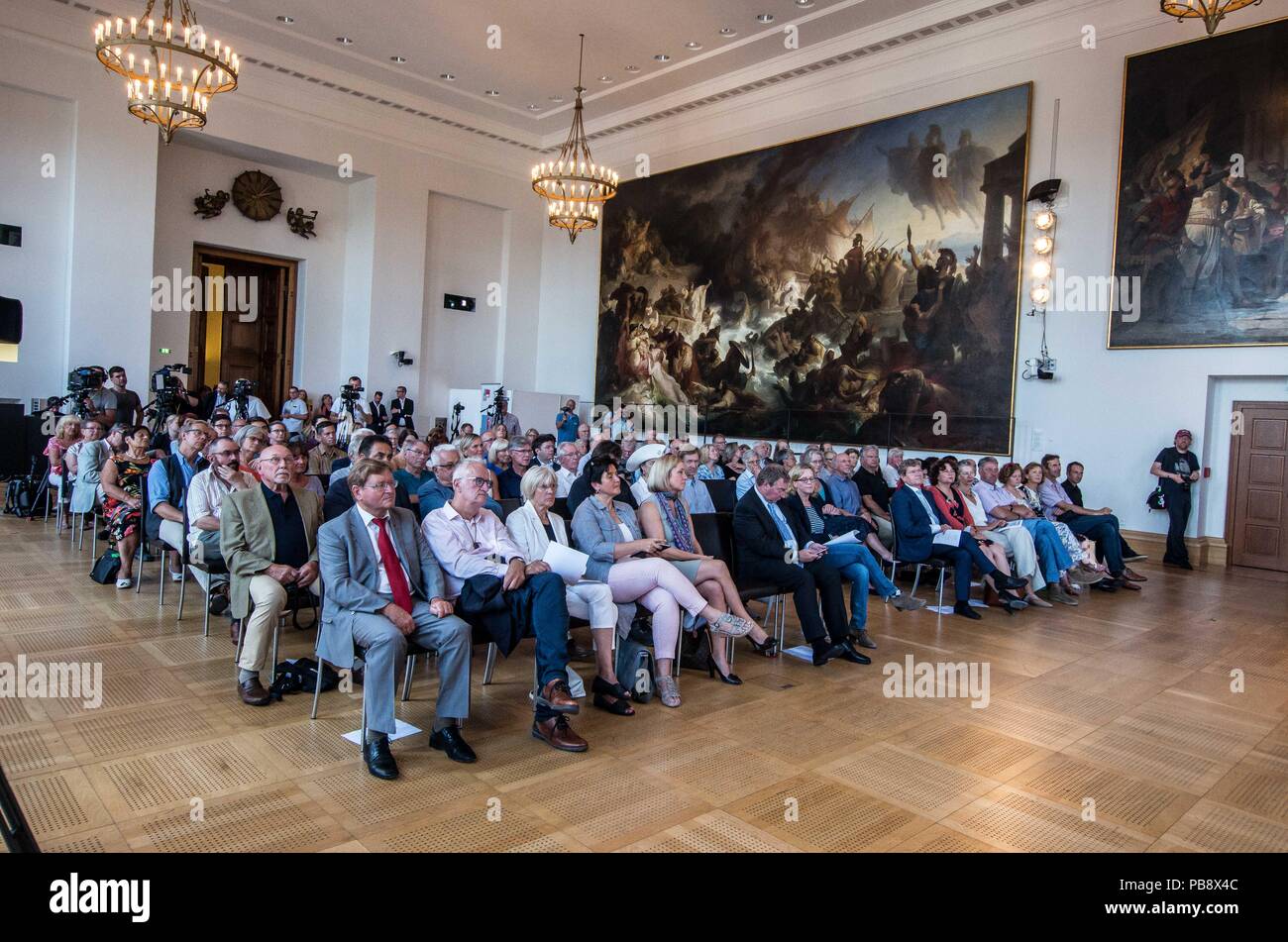 Munich, Bavaria, Germany. 27th July, 2018. Lifeline Captain CLAUS PETER REISCH sits in the first row awaiting his award with a view of drowning people in the artwork on the wall of the Bavarian Landtag. Captain Claus Peter Reisch of the Mission Lifeline NGO received the Europa-Preis (Europe Award) at Bavaria's Landtag (Parliament) for his humanitarian engagement in the Mediterranean in rescuing hundreds migrants in danger of drowning. Reisch was recently arrested in Malta, facing various charges related to the use of the vessel in rescue activities. He is currently out on bail and has surr Stock Photo