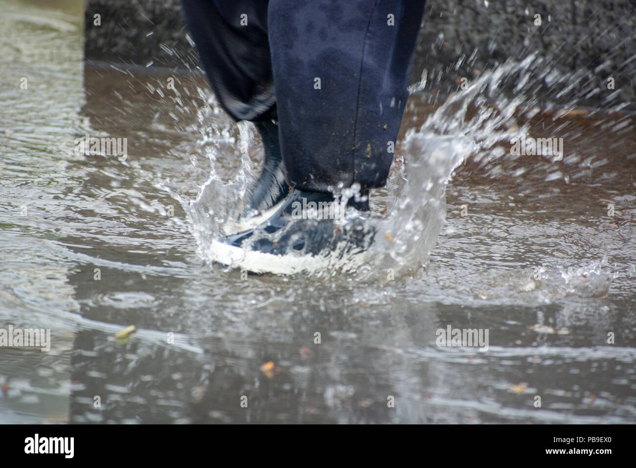 Close-up of kid wearing blue rain boots and walking during sleet, rain and snow on cold day. Child in colorful fashion casual clothes jumping in a pud Stock Photo