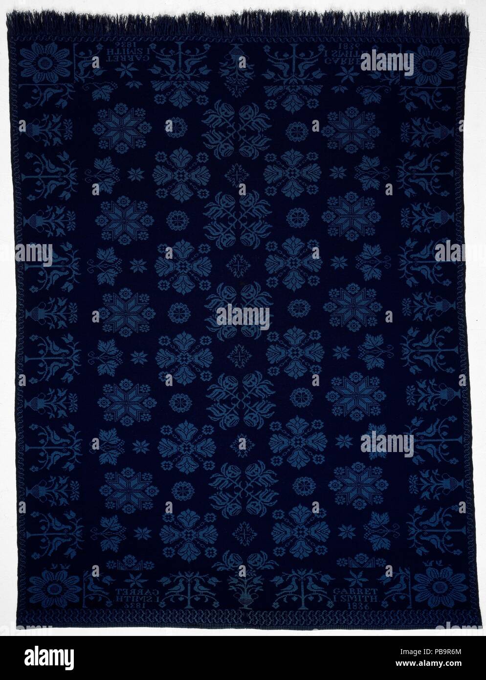 Coverlet. Culture: American. Dimensions: 98 x 71 1/2 in. (248.9 x 181.6 cm). Date: 1836.  This light and dark blue wool double cloth coverlet is woven in two panels and seamed at the center. The ground is decorated with various floral motifs associated with the Dutch weavers of the Bergen County, New Jersey/Rockland County, New York, area. The border is composed of birds and tree motifs alternating with vases of flowers. Each of the four corner blocks is decorated with a single large sunflower. The piece has a natural fringe along the bottom. Museum: Metropolitan Museum of Art, New York, USA. Stock Photo