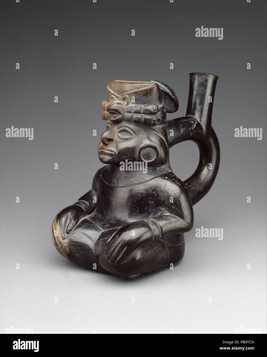 Seated Figure Bottle. Culture: Moche. Dimensions: Overall: 6 3/8 in. (16.19 cm). Date: 2nd-5th century.  The stirrup-spout vessel--so named for the similarity of the spout form to that of a riding saddle stirrup--was a much-favored bottle shape in Precolumbian Peru. It has been suggested that the peculiarity of the double-branch/single-spout shape was to prevent evaporation of the liquids it contained. The stirrup spout was used on ceramic vessels in northern Peru for about twenty-five hundred years. Early in the first millennium B.C., the stirrup-spout bottle was elaborated into sculptural de Stock Photo
