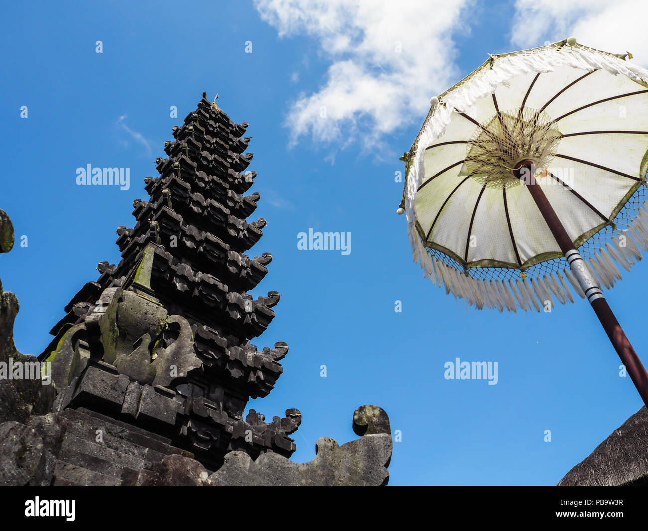 Traditional Balinese temple flanked by a white umbrella against a blue