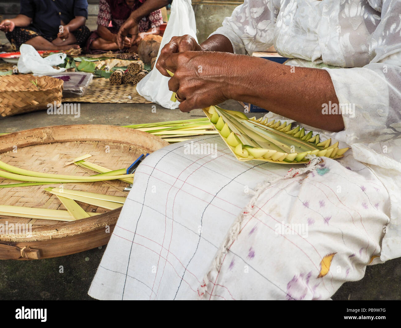 Old woman making bamboo baskets, canang sari, in a local temple in Ubud for Nyepi festival Stock Photo