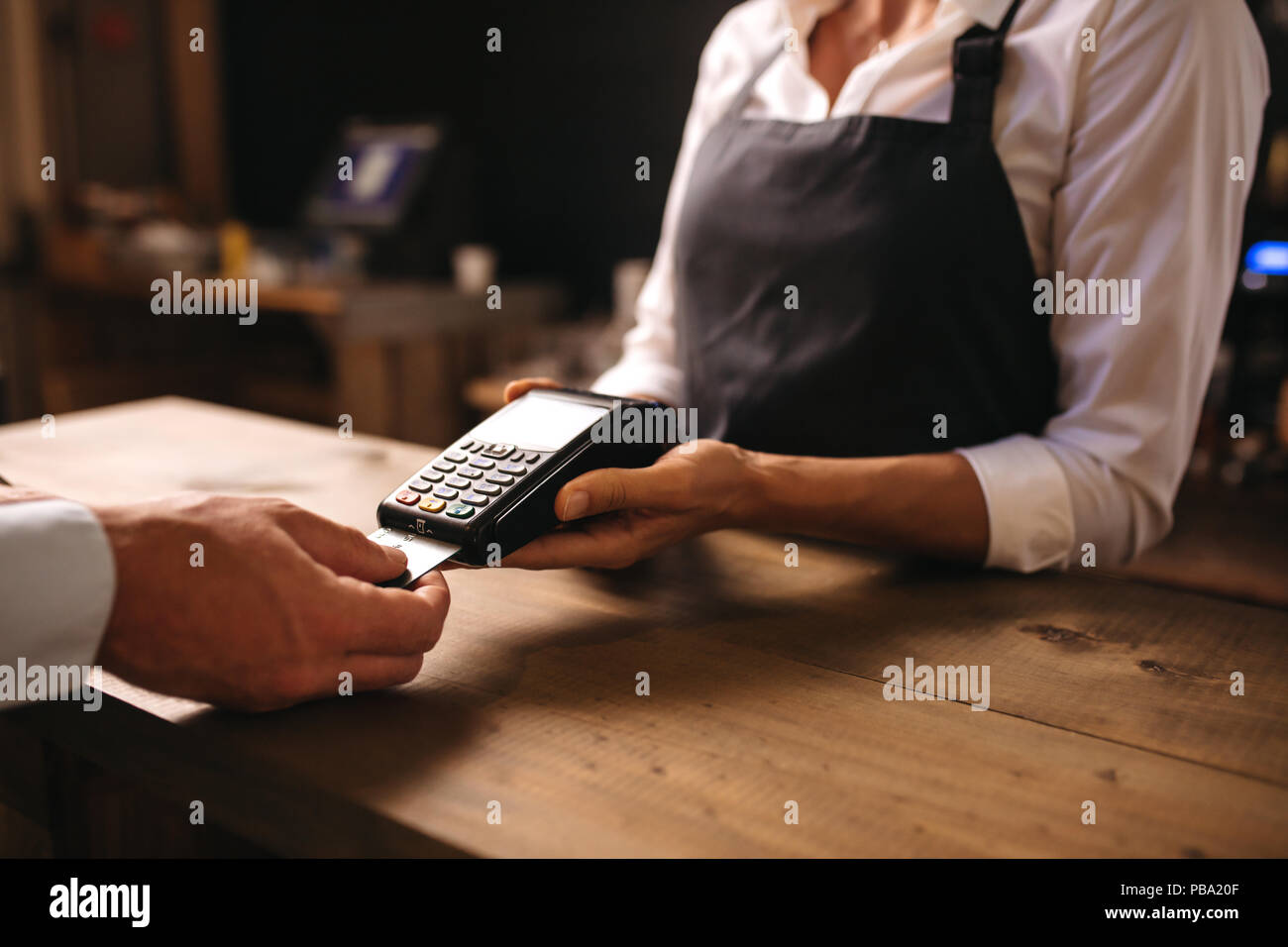 Female bartender holding a credit card reader machine with male customer inserting the card in machine for payment. Stock Photo