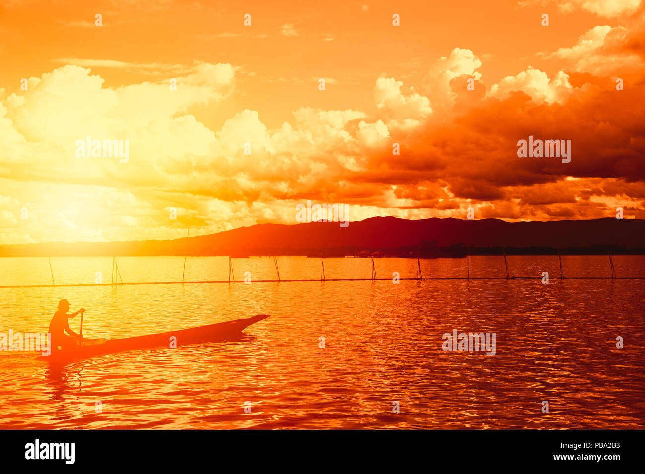 Silhouette man in the wooden boat with beautiful sunset mountain lake countryside view in Phayao, Thailand. Stock Photo
