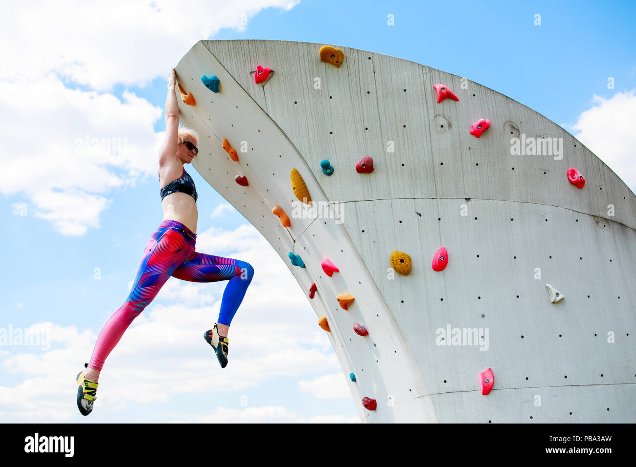 Photo of sporty woman in leggings hanging on wall for rock climbing against  blue sky with clouds in afternoon Stock Photo - Alamy