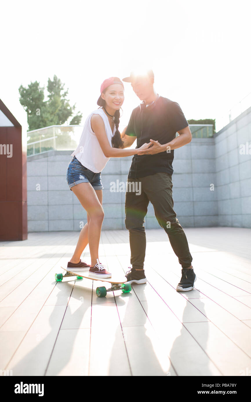 Young Chinese man teaching his girlfriend to skateboard Stock Photo