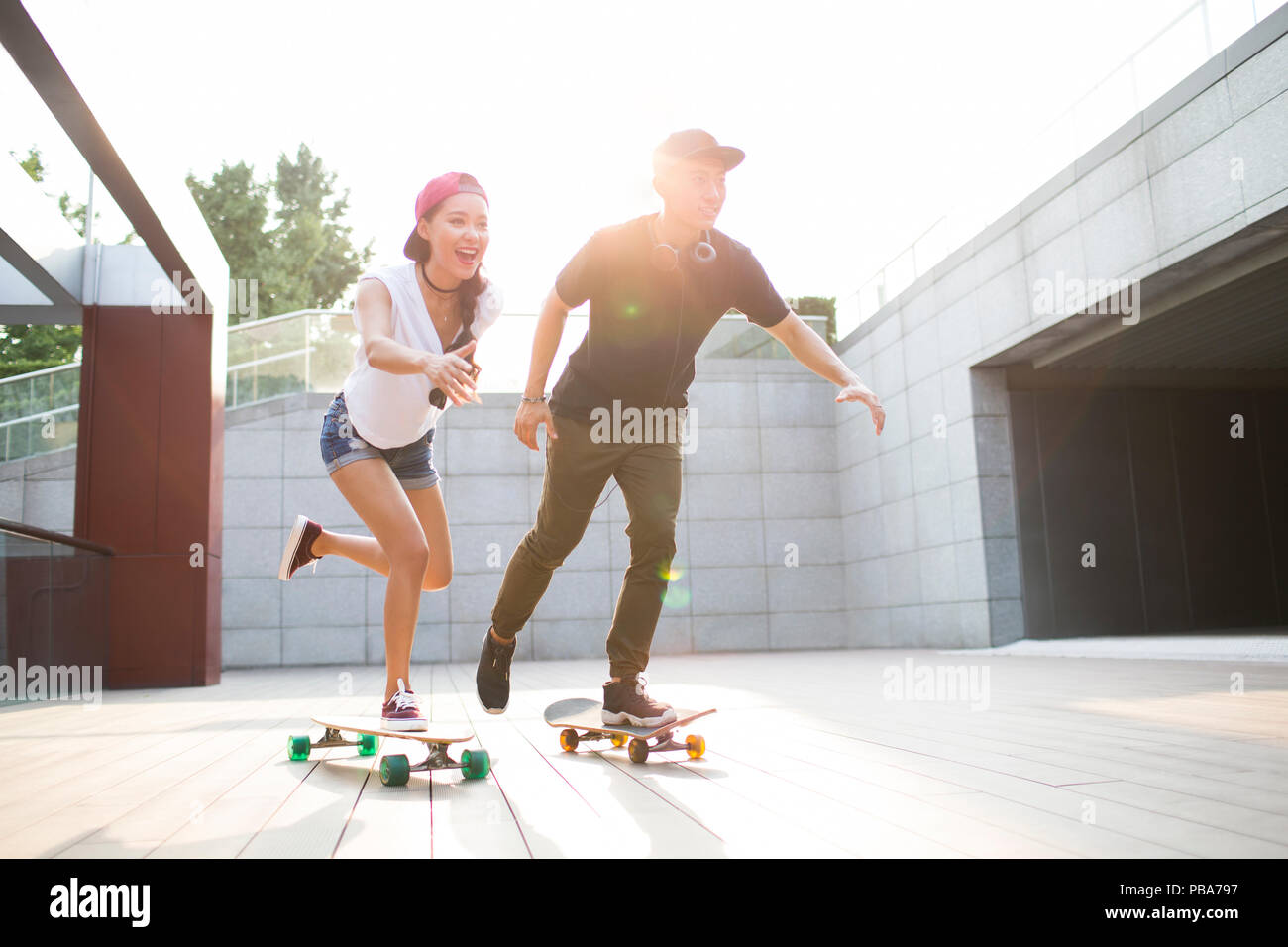 Cheerful young Chinese couple skateboarding Stock Photo
