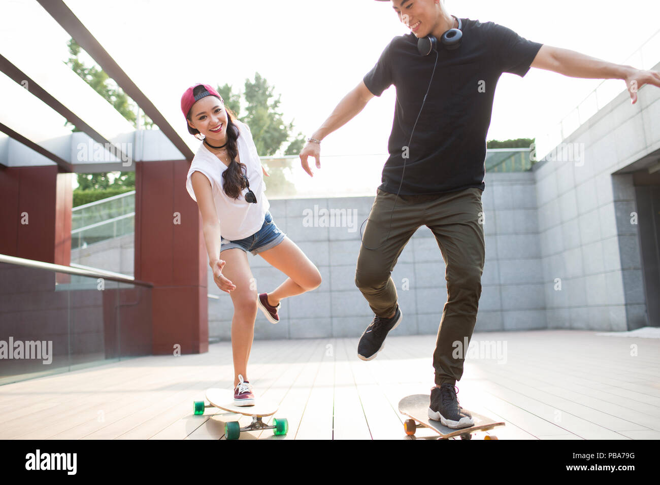 Cheerful young Chinese couple skateboarding Stock Photo