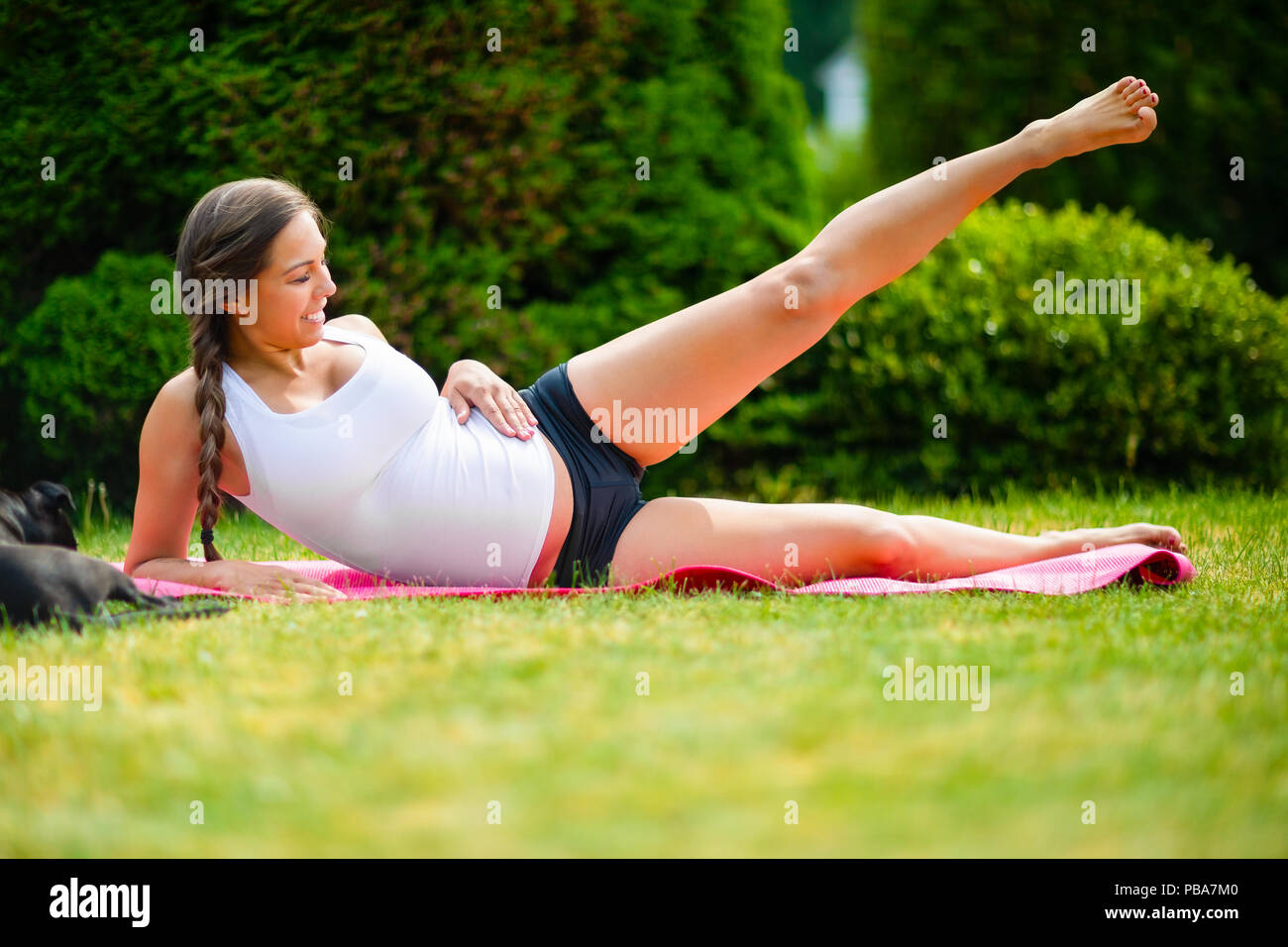 Pregnant woman performing side reclining leg lift while lying on yoga mat in park Stock Photo