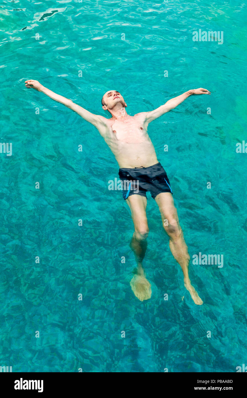 Top view of a young man floating in a swimming pool with open arms