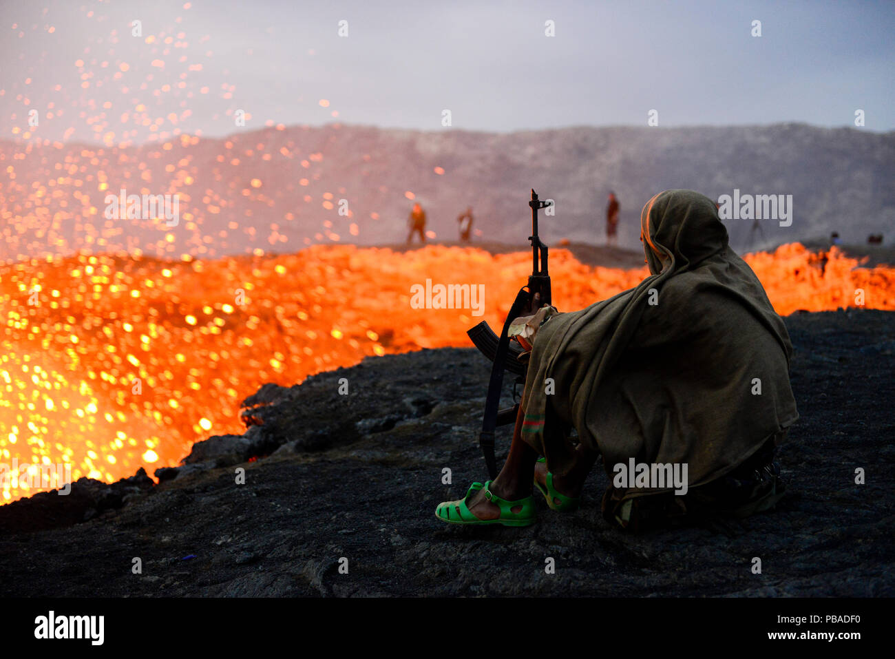 An armed soldier watching activity of Erta Ale volcano crater at dawn. Afar Region, Ethiopia, Africa. November 2014. November 2014. Stock Photo