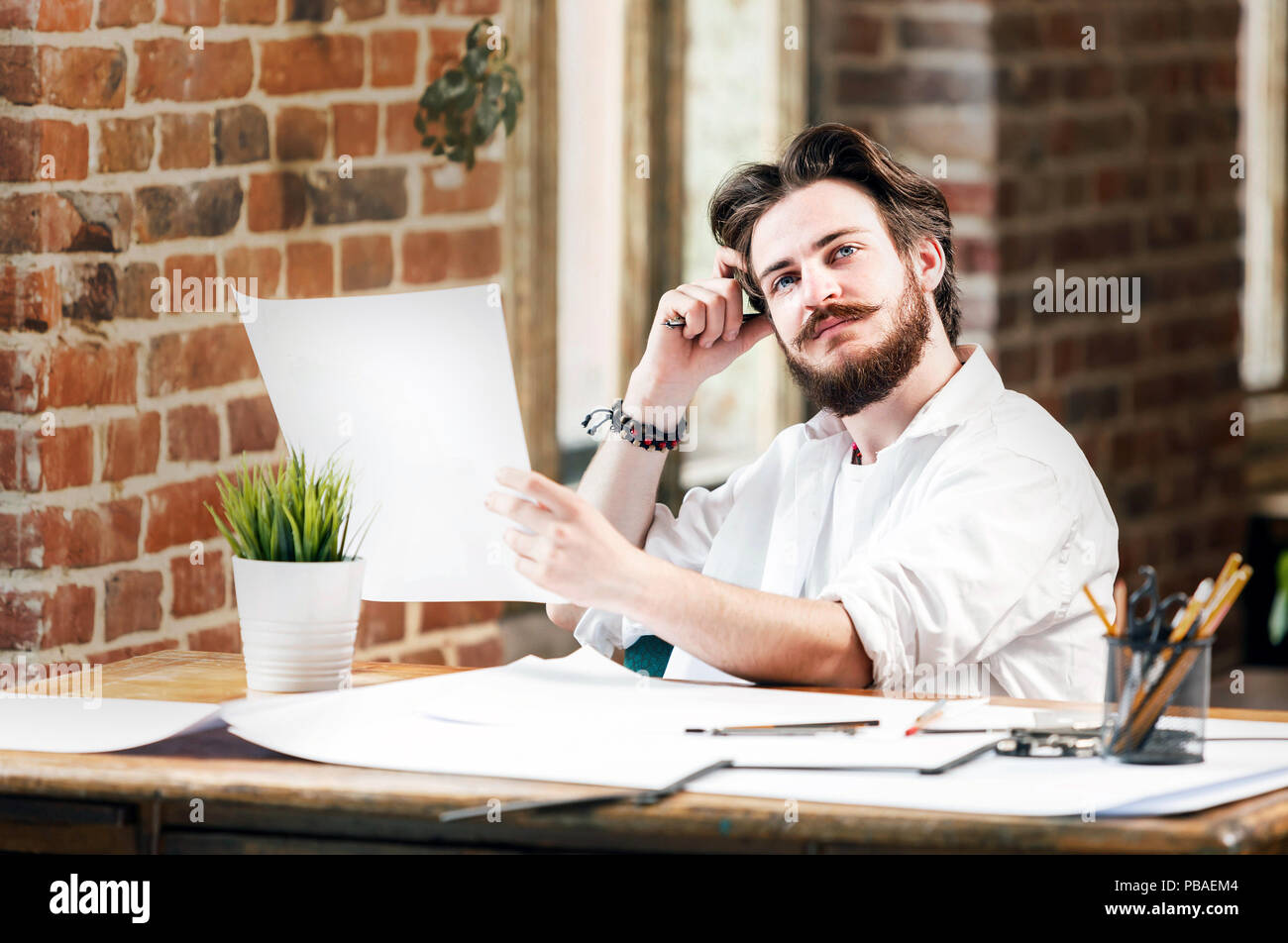 Bearded hipster male architect in white shirt with dividers looking on the blueprint in loft office Stock Photo