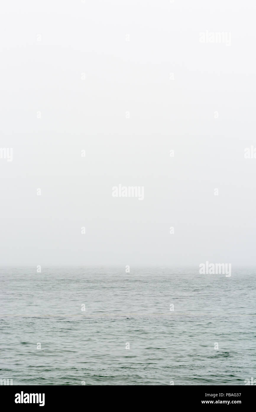 Flat grey sea with wavelets disappearing in the fog. Stock Photo