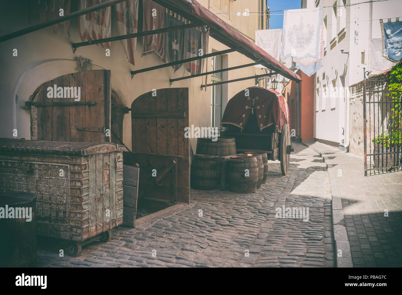 Stylized medieval street with a cart and oak barrels under the standards on the walls in Riga Stock Photo