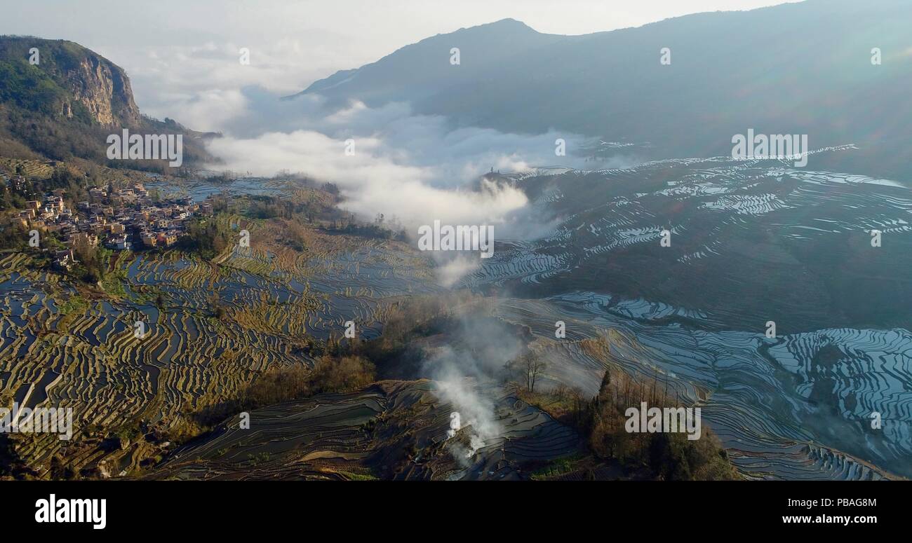 Aerial view on water-filled rice terraces and a valley covered by fog. Yuanyang Rice Terraces early in the morning during spring. Stock Photo