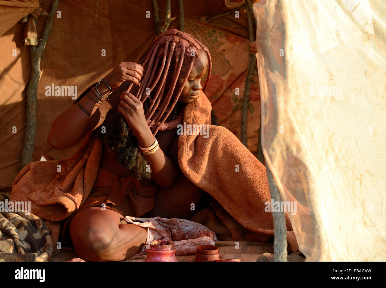 Himba woman applying Otjize (a mixture of butter, ochre and ash) to her hair. Marienfluss Valley. Kaokoland, Namibia October 2015 Stock Photo