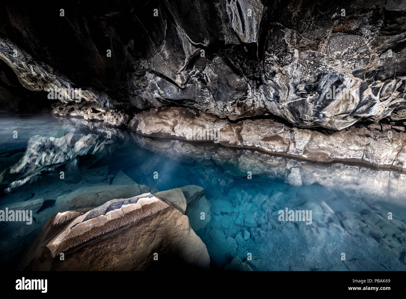 Wide angle view of inside of Grjotagja lava cave near lake Myvatn with hot springs blue, green water, rocks, rocky formations, walls, reflection Stock Photo