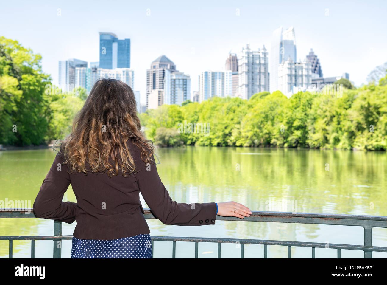Young woman standing in Piedmont Park in Atlanta, Georgia looking at scenery, water, and cityscape skyline of urban city skyscrapers downtown, Lake Cl Stock Photo