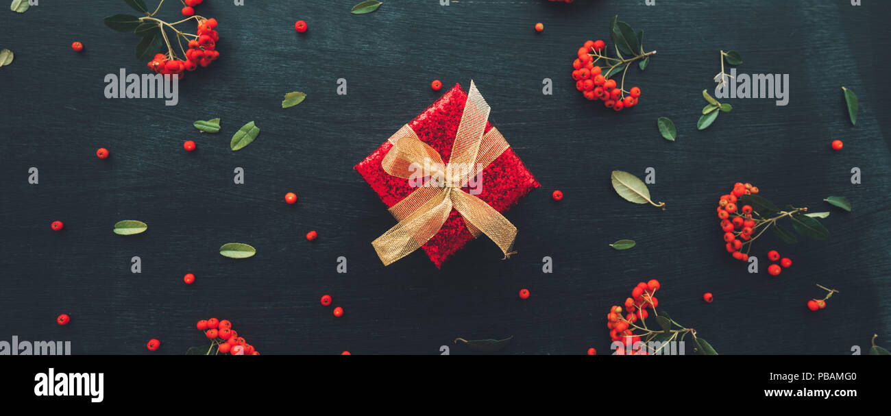 Flat lay anniversary present gift box with red wrapping and golden ribbon on dark background with floral arrangement, top view Stock Photo