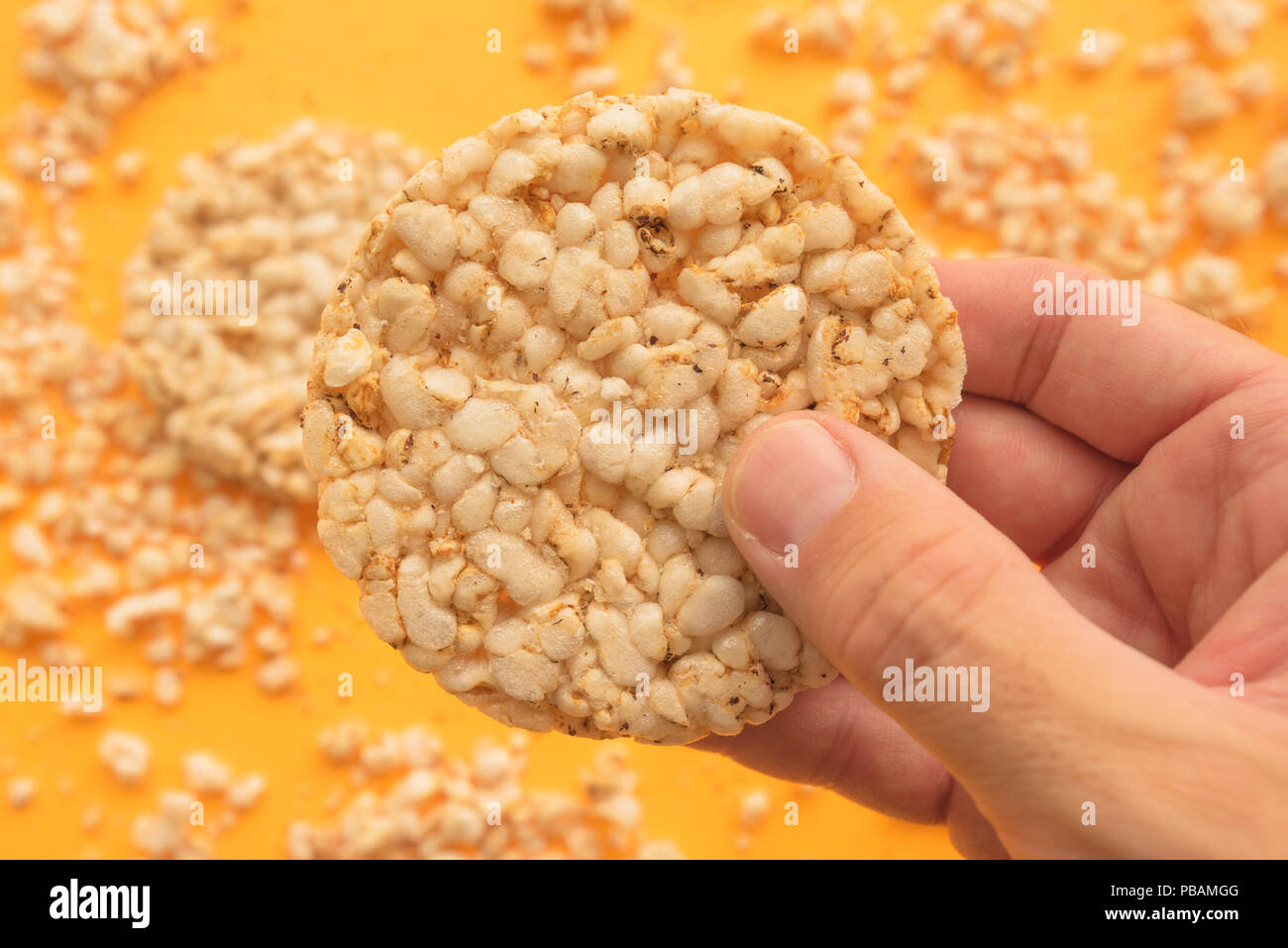 Rice cakes in male hand over yellow background, overhead view Stock Photo