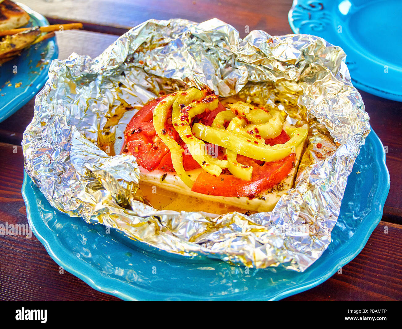 Grilled Feta with tomatoes and peppers in foil. Typical greek Mezze. Stock Photo