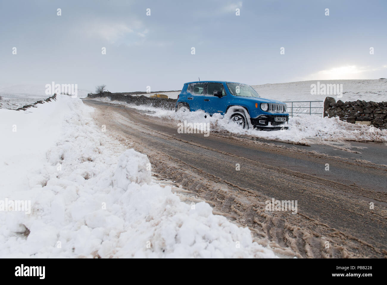 Car abandoned in a snowdrift on a rural road in Cumbria, after a snowstorm. Stock Photo