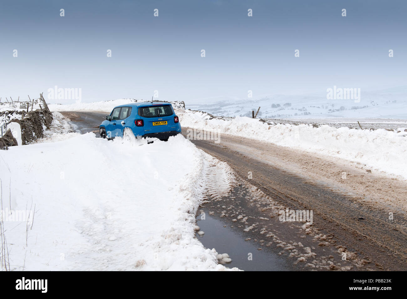 Car abandoned in a snowdrift on a rural road in Cumbria, after a snowstorm. Stock Photo