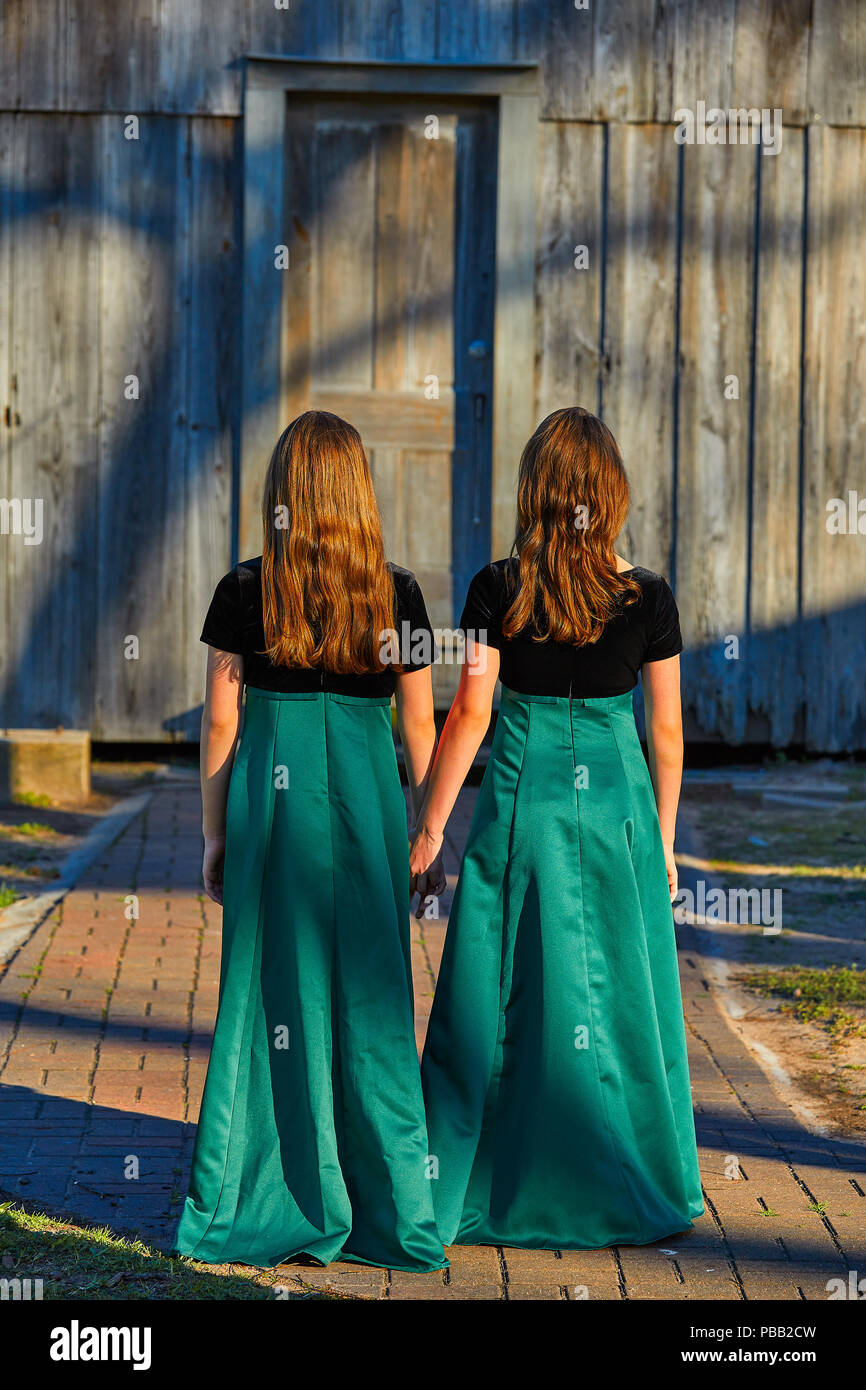 Long dress twin teen sisters hand in hand at the park sooden cabin Stock Photo