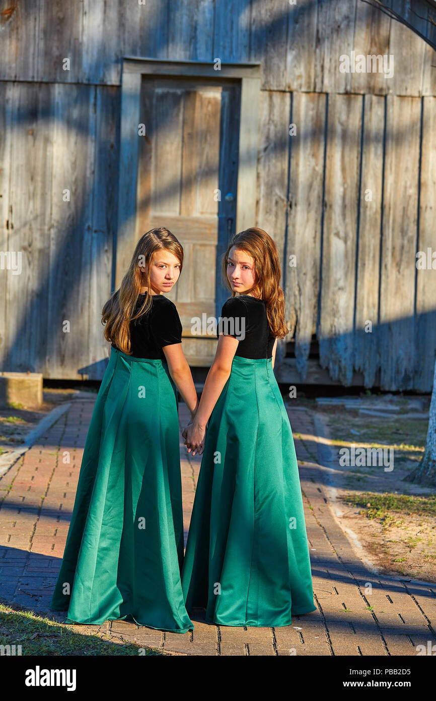 Long dress twin teen sisters hand in hand at the park sooden cabin Stock Photo