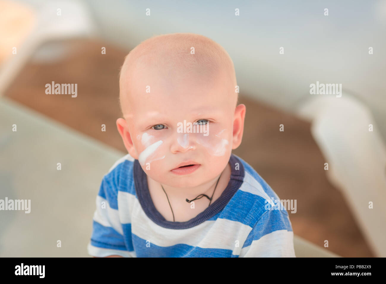 Cute baby boy with sunscreen on holding the bottle of sunscreen lotion