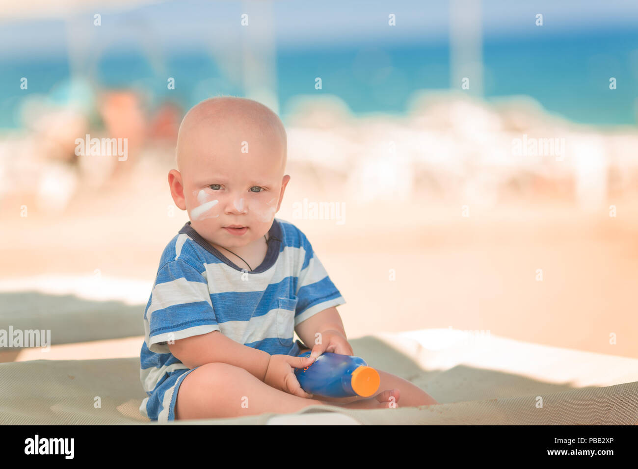 Cute baby boy with sunscreen on holding the bottle of sunscreen lotion