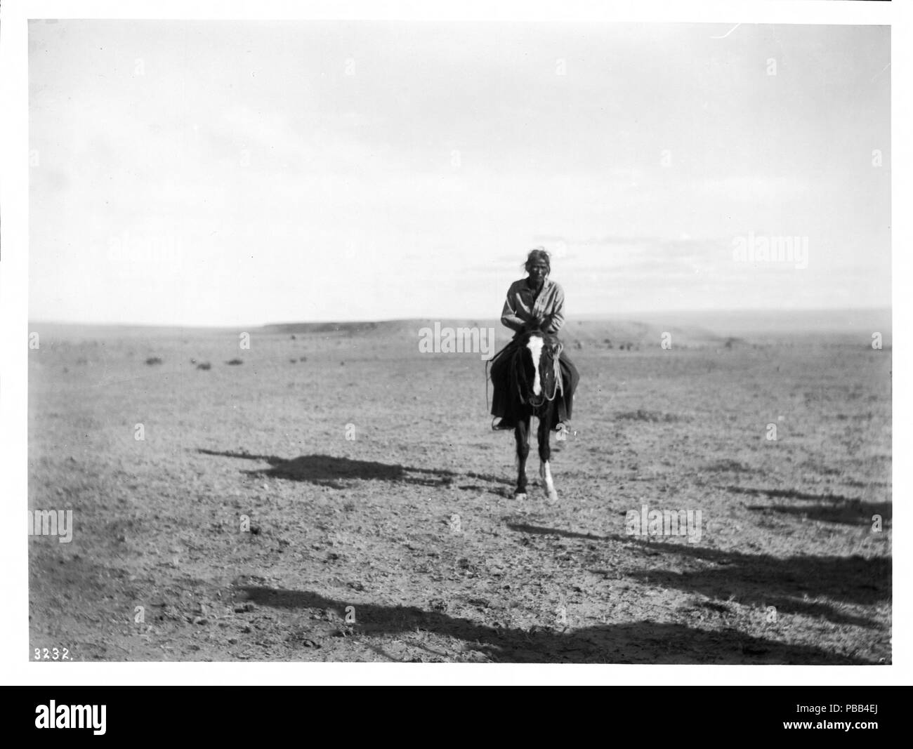. English: Navajo Indian horseman, ca.1900 Photograph of a Navajo Indian horseman, ca.1900. His hands rest across the horn of the saddle as he approaches straight on. He is wearing trousers and a loose shirt. His long dark hair is pulled back behind his head. He and his horse cast a long shadow to the left on the short wildgrass covered flat landscape.  Call number: CHS-3232 Photographer: Pierce, C.C. (Charles C.), 1861-1946 Filename: CHS-3232 Coverage date: circa 1900 Part of collection: California Historical Society Collection, 1860-1960 Type: images Part of subcollection: Title Insurance an Stock Photo