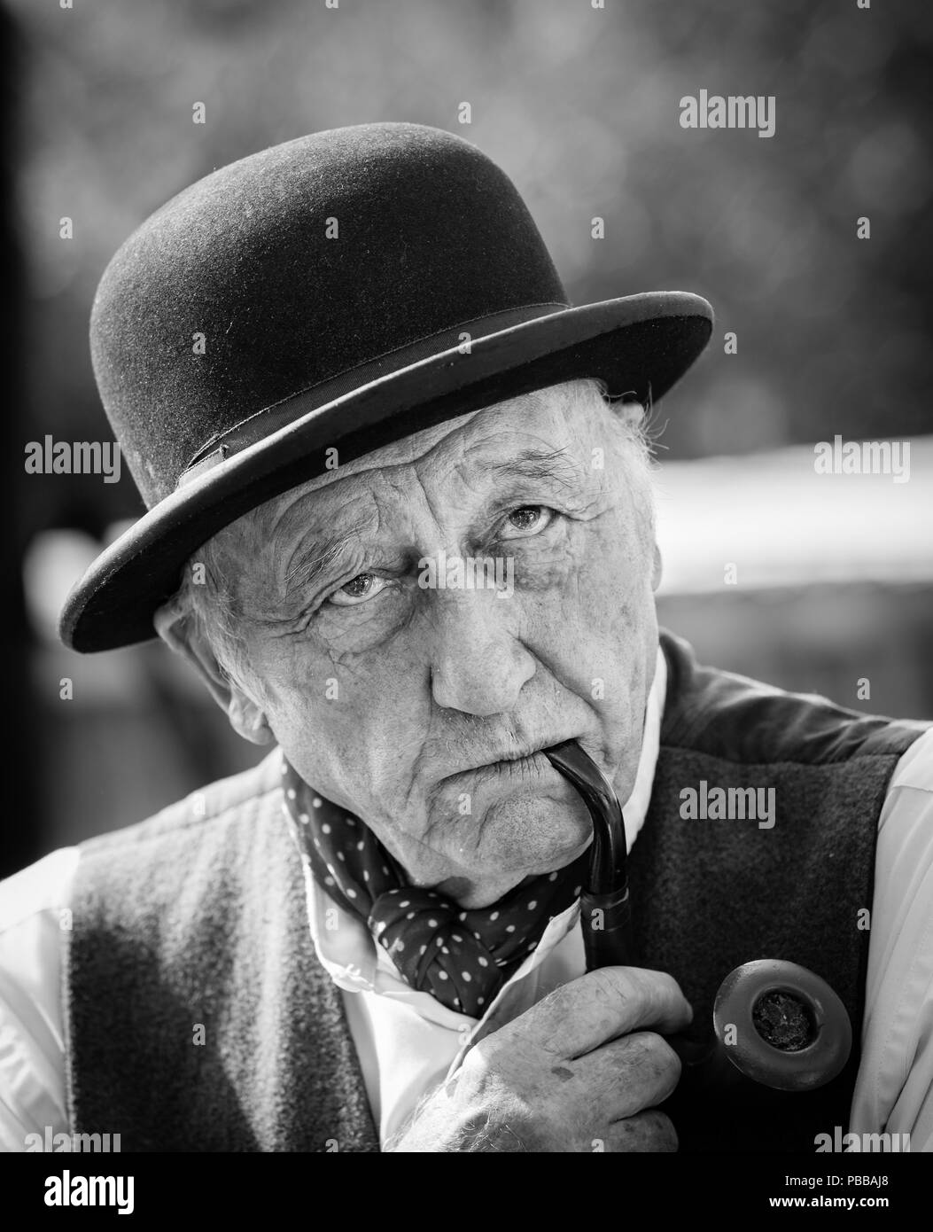 Black & white front view portrait, senior man in black bowler hat smoking pipe, deep in thought, looking serious solemn: UK 1940s. Stock Photo