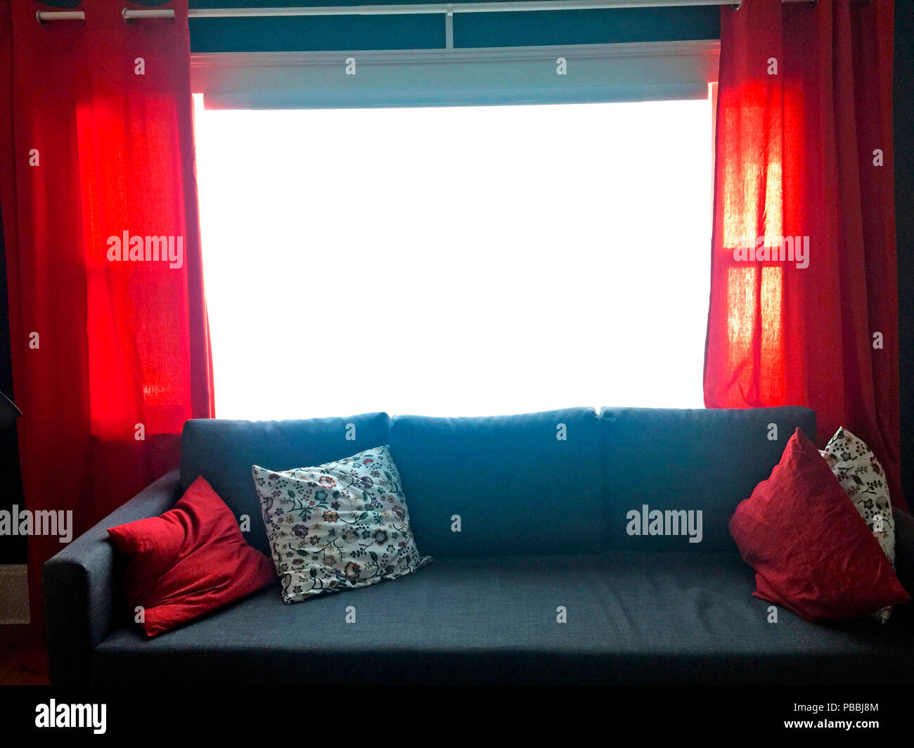 A big picture window with red curtains and red cushions on the chesterfield in the living room of a contemporary home, Halifax, Nova Scotia, Canada Stock Photo