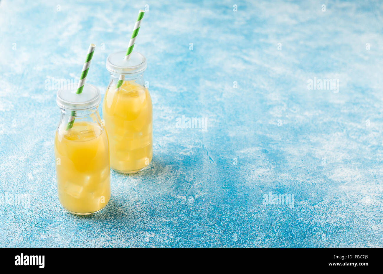 Pineapple cocktail or juice in two glass bottles with straws with ice and two mini pineapples on a blue background Stock Photo