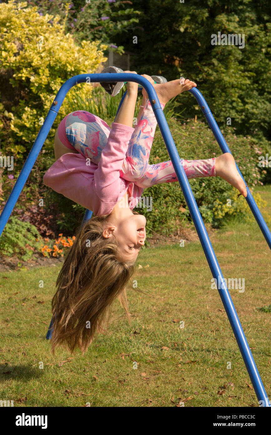 six year old girl doing gymnastics acrobatics on apparatus in back garden for play, UK. Stock Photo