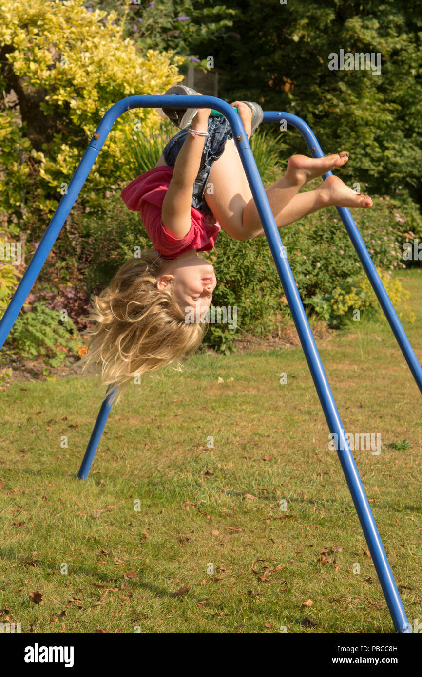 three year old girl doing gymnastics acrobatics on apparatus in back garden for play, UK. Stock Photo