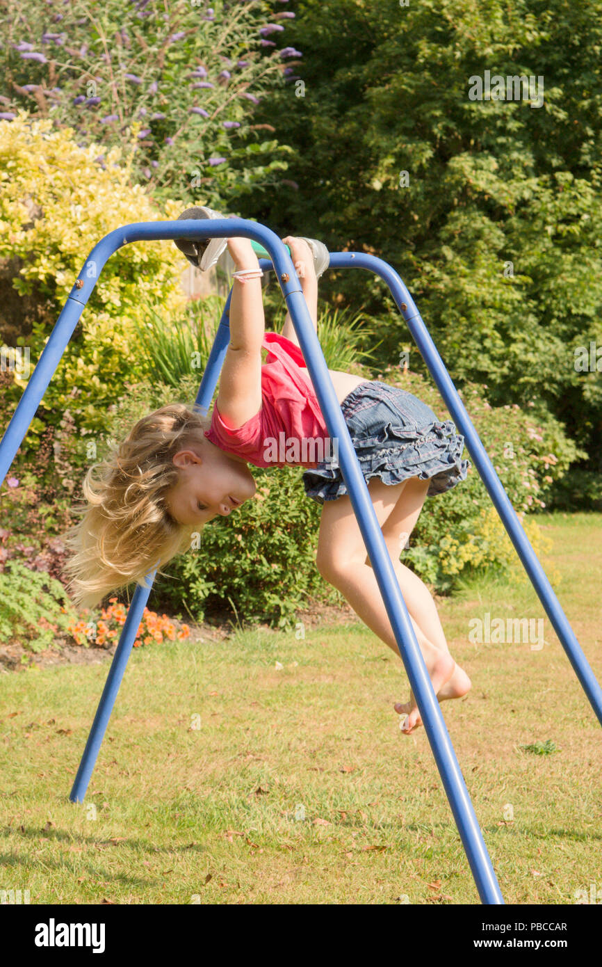 three year old girl doing gymnastics acrobatics on apparatus in back garden for play, UK. Stock Photo