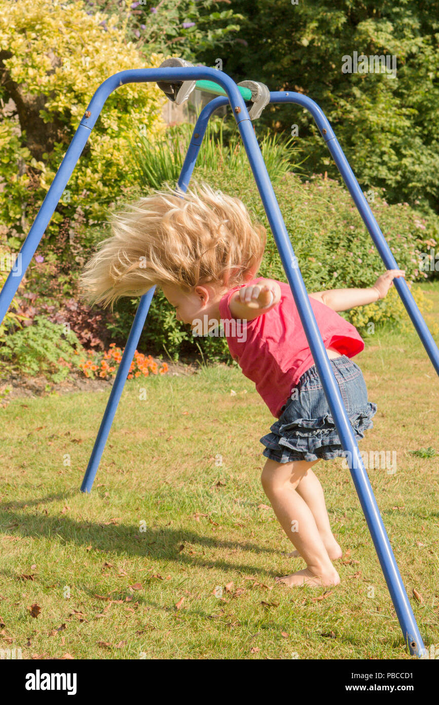 three year old girl doing gymnastics acrobatics on apparatus in back garden for play, UK. Stock Photo