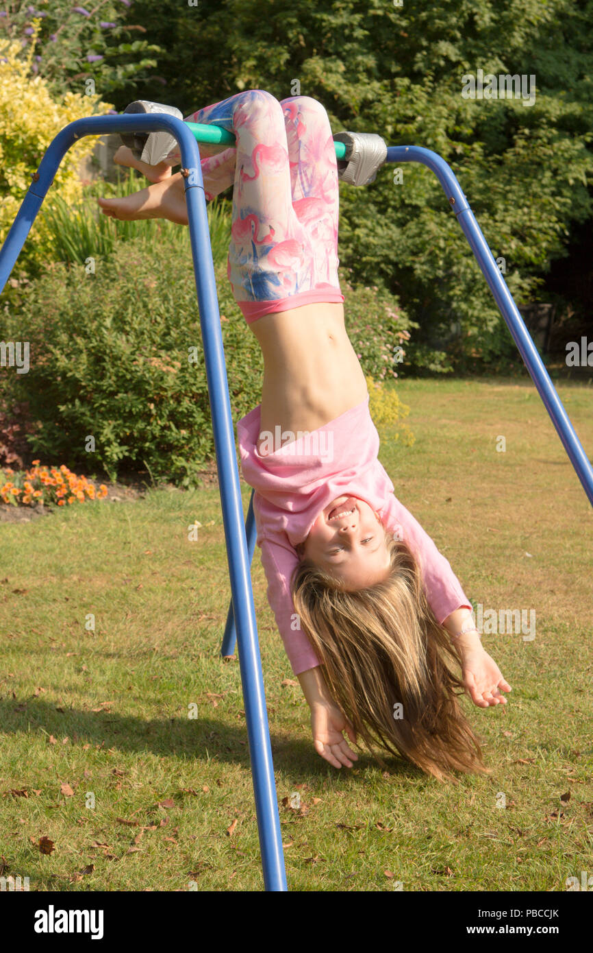 six year old girl doing gymnastics acrobatics on apparatus in back garden for play, UK. Stock Photo