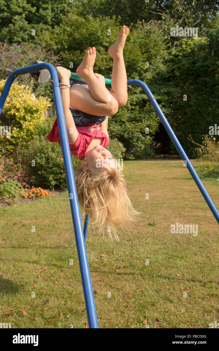 three year old girl doing gymnastics acrobatics on apparatus in back garden for play, UK. Stock Photo