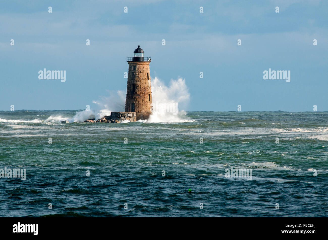 Giant waves surround stone lighthouse tower of Whaleback light as sun breaks through clouds in southern Maine. Stock Photo
