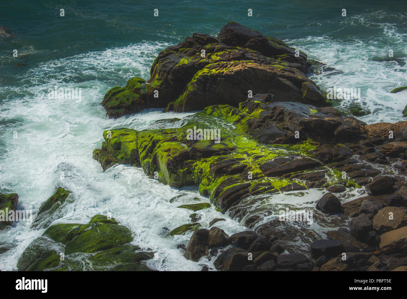 Waves crashing into rock formations covered with green algae, Point Mugu, California Stock Photo